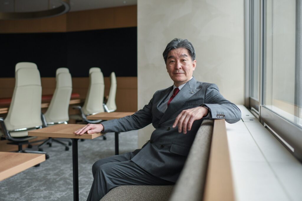 A man in a grey suit sits at a small table by a window.